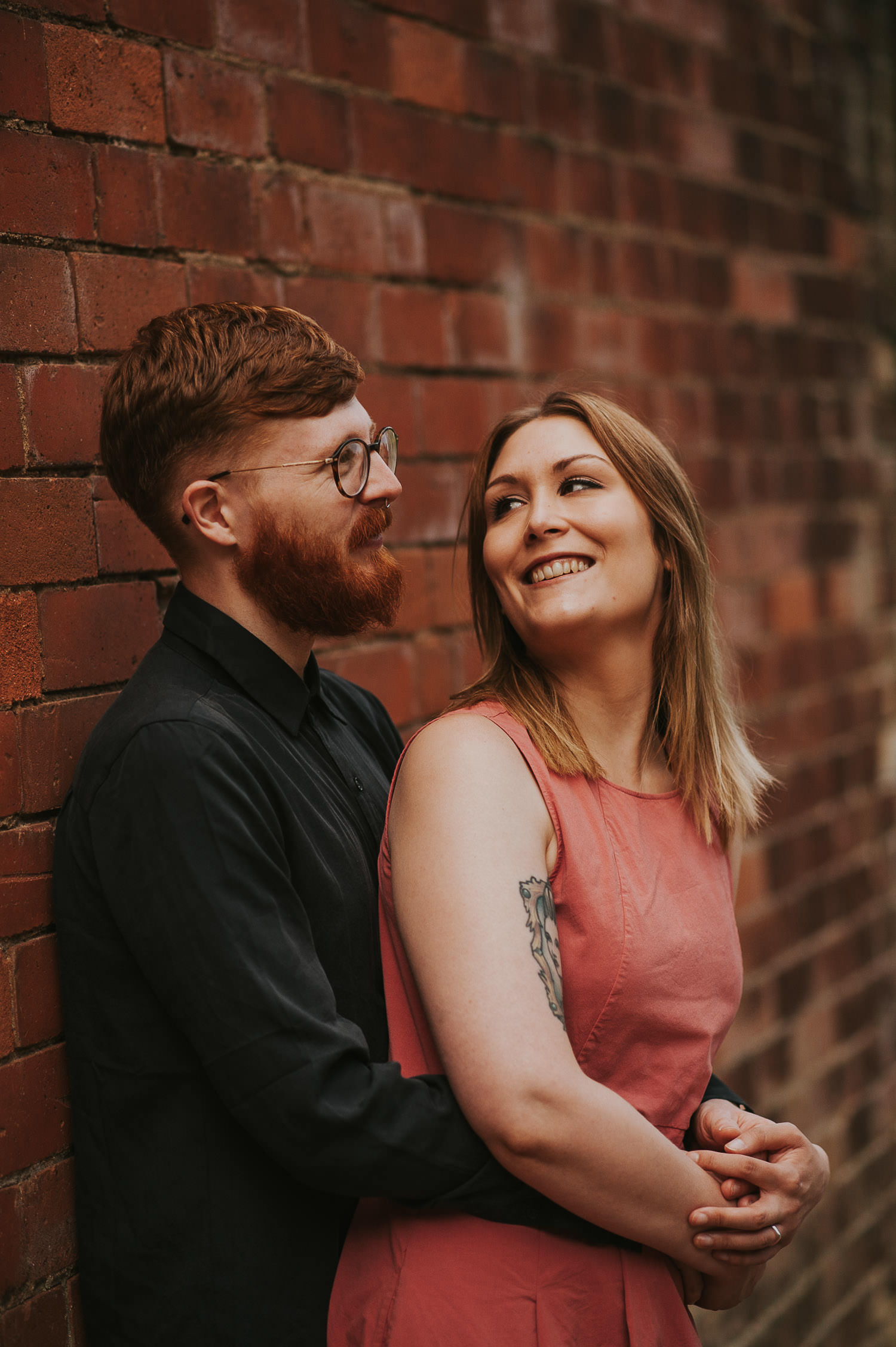 engagement shoot couple leaning agains a red brick wall